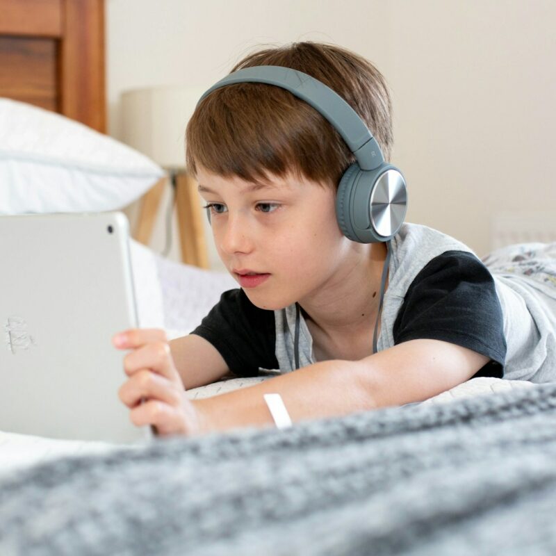boy in blue shirt wearing headphones lying on bed